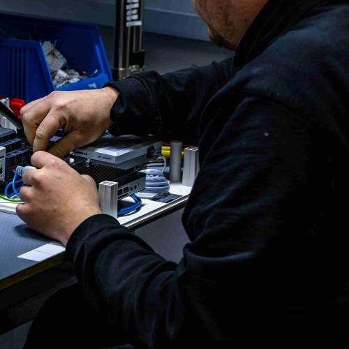 Työntekijä työskentelee käsillään elektroniikkalaitteen parissa.
