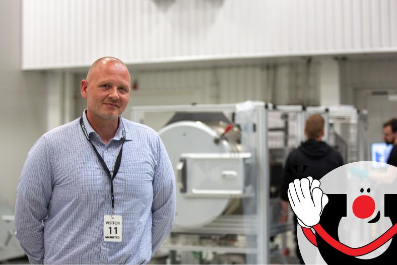 Jani Rank seisoo Manutecin tuotantotiloissa, taustalla näkyy laitteita ja oikeassa alareunassa on Manutecin maskottihahmo.